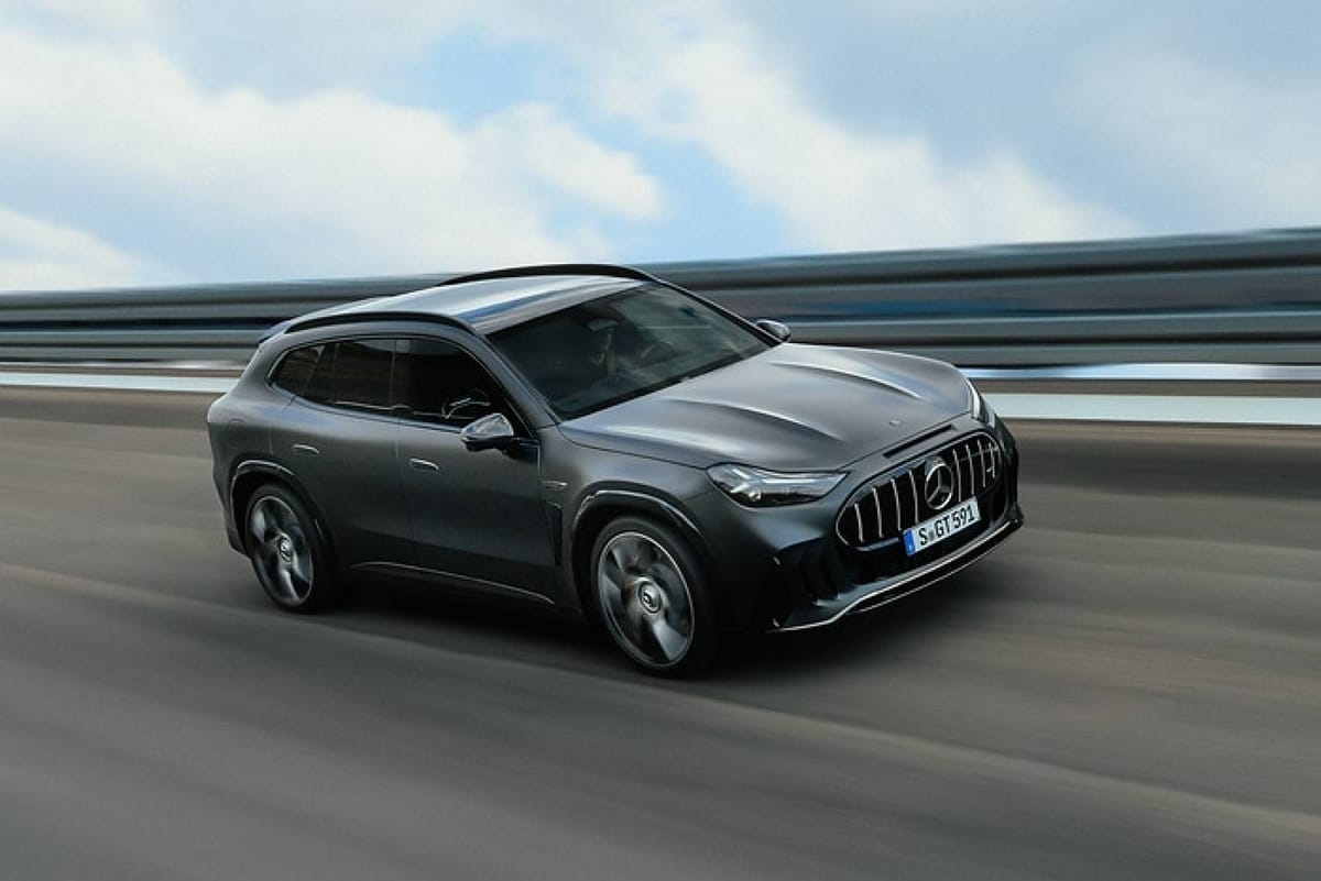 A dark gray Mercedes-AMG GT SUV driving on a road, with a barrier and cloudy sky blurred behind it