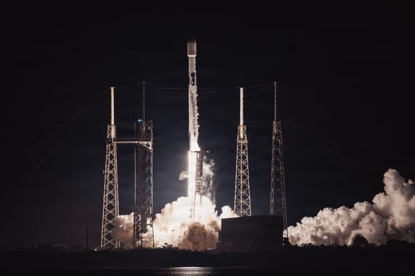 A Falcon 9 rocket lifts off at night between launch-pad towers, its exhaust lighting billowing clouds of steam